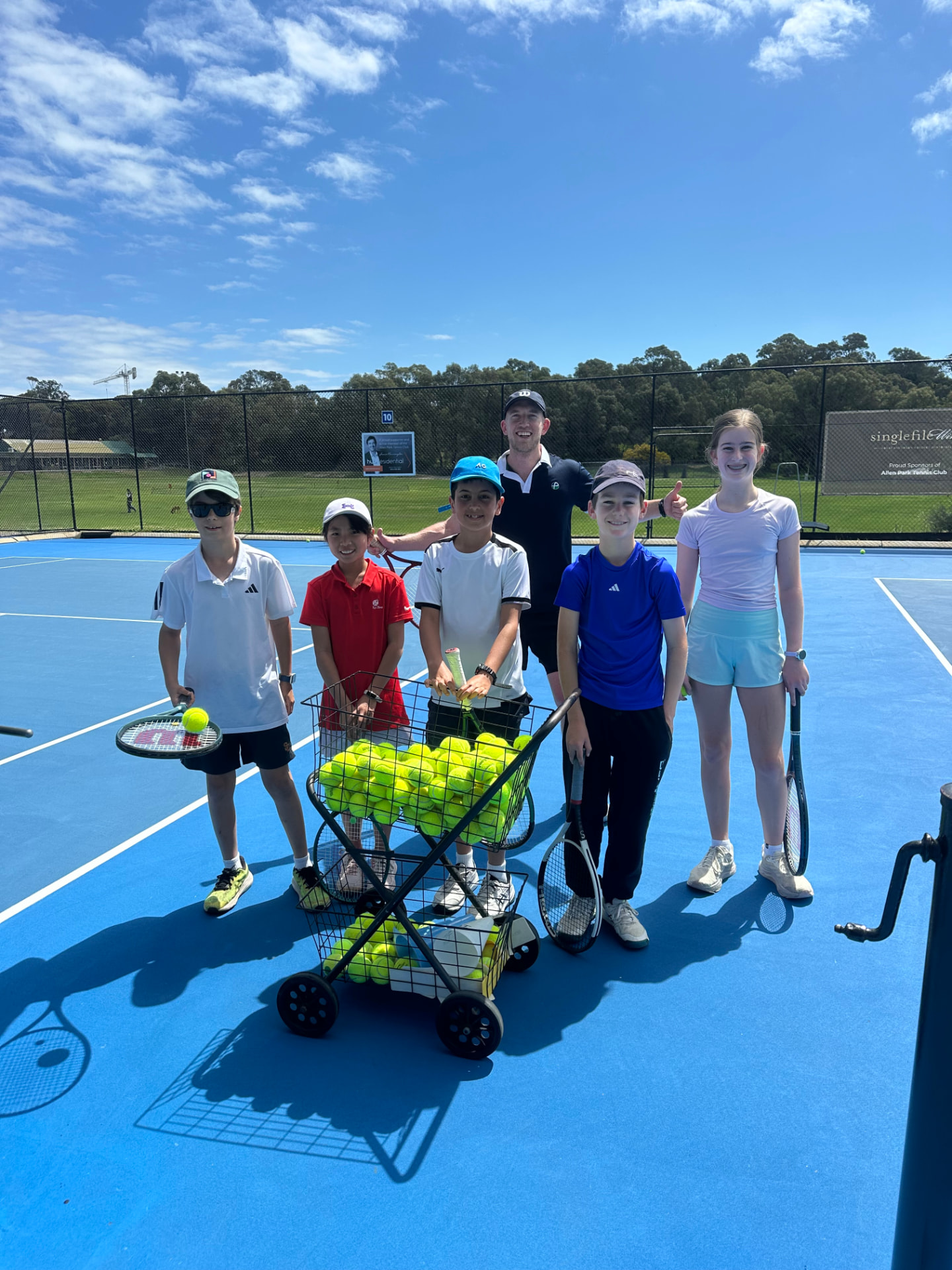 Junior players and a coach with a basket of tennis balls at Allen Park
